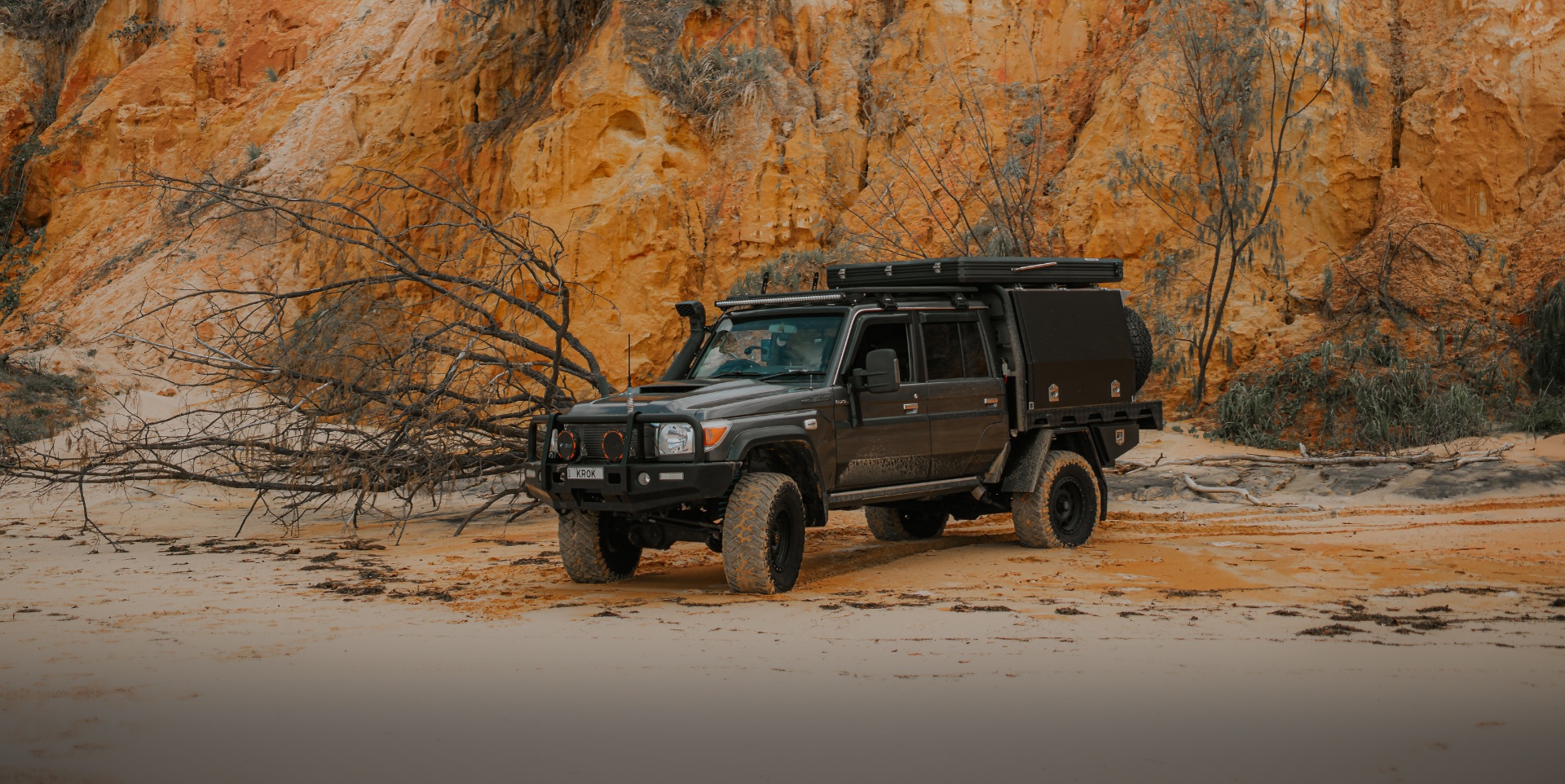 Kitted-out Toyota Land Cruiser tray-back parked against ochre cliffs in the Australian outback